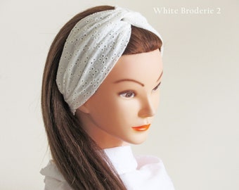 May include: White eyelet fabric turban headband. The headband is twisted and knotted at the top.