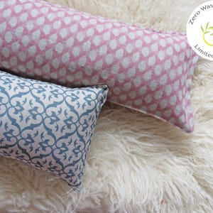 May include: Two decorative throw pillows, one with a pink and white floral pattern and the other with a blue and white geometric pattern. The pillows are on a white fluffy surface. The text on the label reads "Zero Waste Materials Limited Quantity".