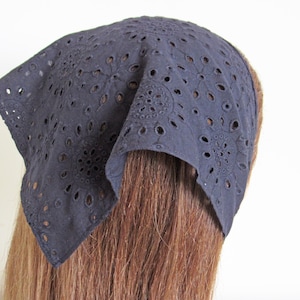 May include: A dark blue eyelet headband, featuring a square shape and intricate floral cut-out patterns. The headband is made of a soft fabric and is worn on the head, covering the top of the head and forehead. This accessory is perfect for adding a touch of style.