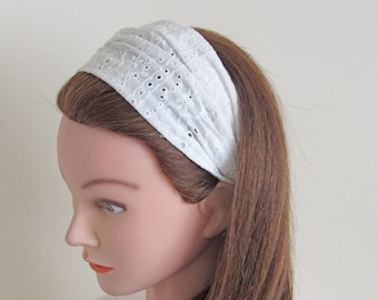 May include: White eyelet headband with a gathered design. The headband is made of a soft, stretchy fabric and is perfect for adding a touch of elegance to any outfit.