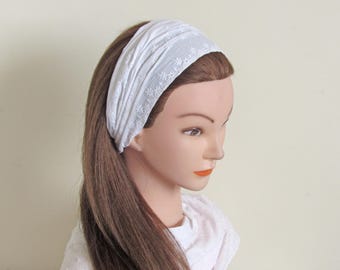 May include: A white headband with an embroidered floral pattern is worn on a mannequin with long brown hair. The headband is wide and covers the forehead, with the floral design adding a delicate touch to the accessory.