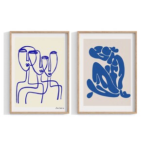 K&ouml;nnte beinhalten: Zwei gerahmte Drucke mit abstrakten Linienzeichnungen in Blau auf cremefarbenem Hintergrund. Der erste Druck zeigt drei Gesichter, der zweite Druck zeigt eine einzelne Figur.