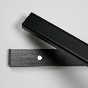 May include: Black wooden shelf bracket with a single screw hole. The bracket is made of wood with a black finish.