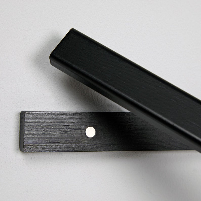 May include: Black wooden shelf bracket with a single screw hole. The bracket is made of wood with a black finish.