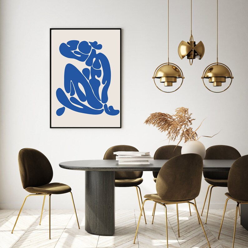 Pu&ograve; includere: Una stampa artistica incorniciata con una figura astratta blu su sfondo crema. L'opera &egrave; appesa sopra un tavolo da pranzo grigio scuro con sedie in velluto marrone e gambe dorate. Lampade a sospensione dorate sopra il tavolo.