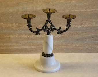 May include: A white marble candle holder with three gold candle cups and an ornate metal design.