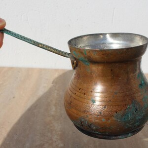 May include: A small, copper coffee pot with a long handle. The pot has a worn, aged patina and is slightly tarnished.