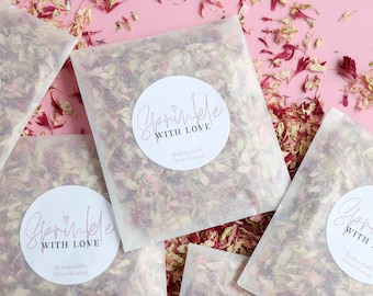Può includere: Quattro sacchetti di carta bianca pieni di petali di fiori rosa e bianchi. Ogni sacchetto ha un adesivo rotondo con il testo "Sprinkle with Love" e "Confetti di fiori biodegradabili".