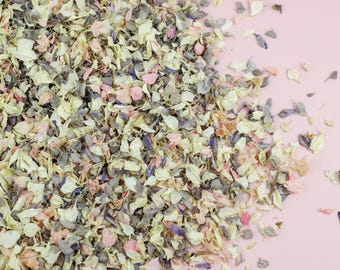 Könnte beinhalten: Ein Haufen getrockneter Blütenblätter in Rosa-, Weiß- und Blautönen. Die Blütenblätter sind auf einem rosa Hintergrund verstreut.