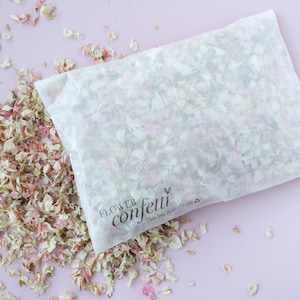 May include: A white paper bag filled with pink and white flower petals. The bag has a black label that says "FLOWER confetti" with a heart symbol and the text "This bag is recyclable."