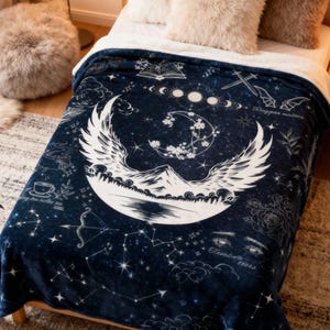 以下が含まれることがあります： 三日月、翼、山、星座を特徴とする白い天体デザインの濃い青色の毛布。 毛布は、ふわふわの枕とラグが付いた木製のベッドの上にあります。