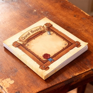 May include: A stack of square notepads with a "Quest Board" design. The design features a parchment-style background with a wooden frame, a scroll banner, a wax seal, and a small sword. The notepad is sitting on a wooden table.