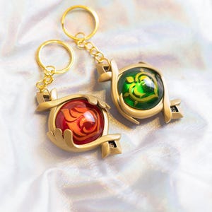 May include: Two gold keychains with red and green glass charms. The charms are shaped like hearts and have intricate designs.