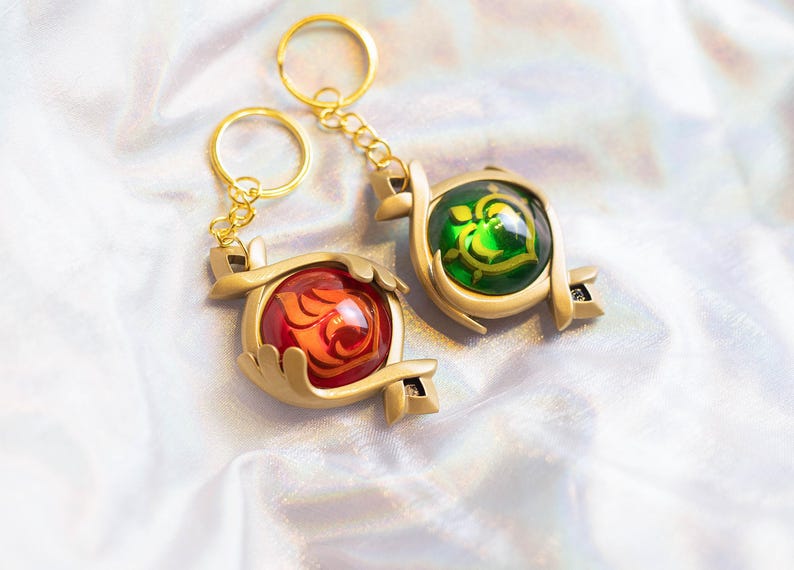 May include: Two gold keychains with red and green glass charms. The charms are shaped like hearts and have intricate designs.