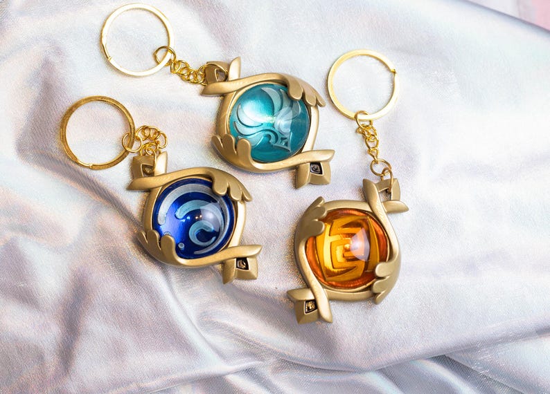 May include: Three gold keychains with different colored glass orbs. Each orb has a different design inside. The keychains are on a silver background.