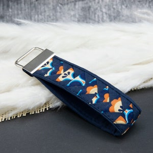 Könnte beinhalten: Ein marineblaues Schlüsselband mit einem geometrischen Blumenmuster in Orange, Hellblau und Weiß. Der Stoff ist gesteppt. Das Schlüsselband hat ein silberfarbenes Metallrechteck zum Befestigen von Schlüsseln.