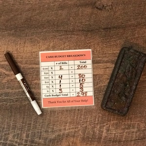 May include: A white sheet of paper with a red border and the text "CASH BUDGET BREAKDOWN" printed on it. The paper has a table with the headings "# of Bills" and "Total". The table lists different denominations of bills and the number of each bill. The total amount of each denomination is calculated and listed in the "Total" column. The total cash budget is $298.