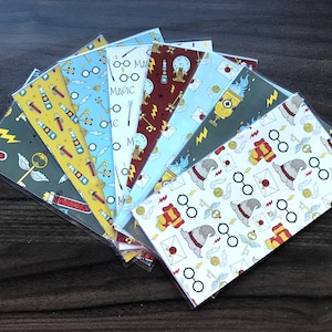 May include: A set of eight Harry Potter themed bookmark designs. The designs feature various magical objects and symbols, including glasses, wands, potions, and a Hogwarts hat. The bookmarks are printed on white cardstock and have a glossy finish.
