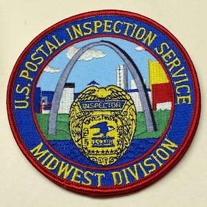 Op de afbeelding: Een blauwe en rode ronde patch met de tekst "U.S. Postal Inspection Service Midwest Division" rond de rand. Het midden van de patch toont een gestileerd beeld van de Gateway Arch in St. Louis, Missouri, met een gouden postinspecteurbadge op de voorgrond.