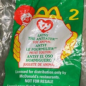 Pode incluir: Saco plástico verde selado com um brinquedo Happy Meal do McDonald's. O saco tem um design amarelo e branco com o texto "ANTSY THE ANTEATER" e o número "2". O saco também inclui o texto "NÃO PARA REVENDA".