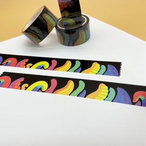 May include: Two rolls of black and white patterned washi tape with colorful abstract designs. The tape is unrolled on a white surface.