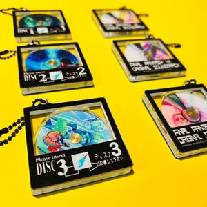 May include: Several Final Fantasy VI Original Soundtrack CD keychains. Each keychain features a colorful CD design inside a black and clear plastic case. The cases have the text "DISC" and "Please insert DISC" printed on them.