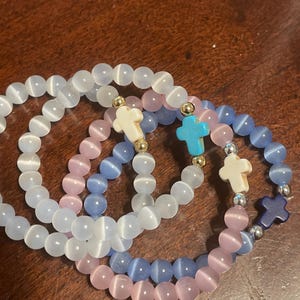 May include: Three beaded bracelets with cross charms. The bracelets are white, blue, and pink.