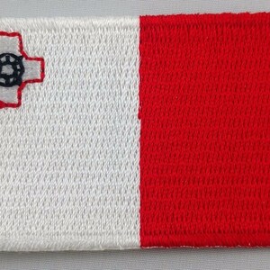 May include: A white and red embroidered patch featuring the Maltese cross and a red shield with a white circle in the centre.