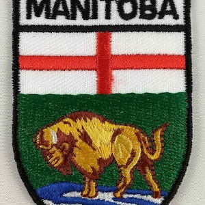 May include: Embroidered patch featuring the coat of arms of Manitoba, Canada. The patch is shaped like a shield and features a white background with a red cross, a green field with a brown bison, and a blue and white water feature at the bottom. The text "MANITOBA" is displayed in black at the top of the patch.