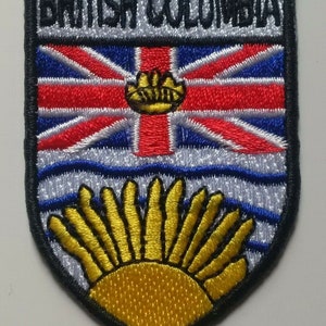 Peut inclure: Un écusson brodé noir et blanc avec le texte "BRITISH COLUMBIA" en haut. L'écusson présente un drapeau britannique rouge, blanc et bleu avec une couronne dorée au centre. Sous le drapeau, un motif de vagues blanches et bleues avec un soleil doré se levant du bas.