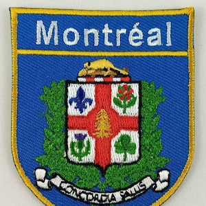 May include: A blue and gold embroidered patch with the word "Montréal" at the top and a coat of arms in the center. The coat of arms features a red cross with a white background and various symbols, including a fleur-de-lis, a tree, and a thistle. The words "Concordia Salus" are written on a scroll at the bottom of the patch.