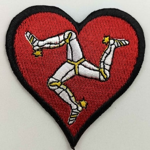 Könnte beinhalten: Roter herzförmiger Patch mit einem weißen gestickten dreibändigen Symbol, bekannt als 'Drei Beine des Mannes', auf rotem Hintergrund.