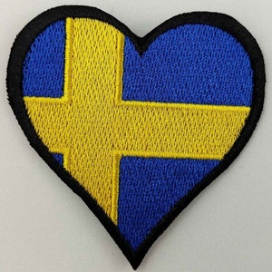 May include: A heart-shaped embroidered patch with the Swedish flag. The flag is blue with a yellow cross.