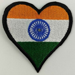 May include: An embroidered heart-shaped patch featuring the Indian flag. The flag is composed of three horizontal stripes: saffron, white, and green. The white stripe features a navy blue wheel with 24 spokes, known as the Ashoka Chakra.
