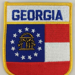 Peut inclure: Un écusson brodé or avec un drapeau de l'État de Géorgie rouge, blanc et bleu. Le drapeau représente un dôme doré avec des piliers et treize étoiles blanches sur un fond bleu. Les mots "GEORGIA" sont brodés en bleu sur un fond blanc en haut de l'écusson.