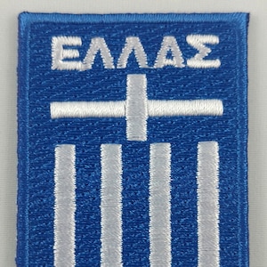 May include: A blue embroidered patch featuring the Greek flag and the word "ΕΛΛΑΣ" in white.