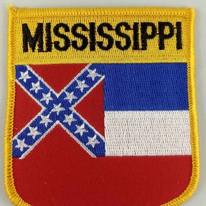 May include: A yellow embroidered patch with the word "MISSISSIPPI" in black lettering. The patch features the state flag of Mississippi, which includes a red field with a blue canton and a white cross with 13 white stars.