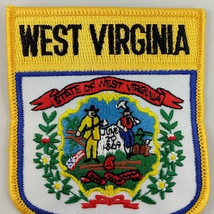 Könnte beinhalten: Ein gestickter Aufnäher in Gelb und Blau mit der Aufschrift "WEST VIRGINIA" in schwarzen Buchstaben. Der Aufnäher zeigt das Staatssiegel von West Virginia, das zwei Männer mit einem Hammer und einer Spitzhacke, ein Band mit der Aufschrift "STATE OF WEST VIRGINIA" und einen Kranz aus grünen Blättern und weißen Blüten zeigt.
