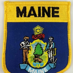 May include: An embroidered patch featuring the state seal of Maine, with the words "MAINE" in black lettering, on a blue background with a yellow border.