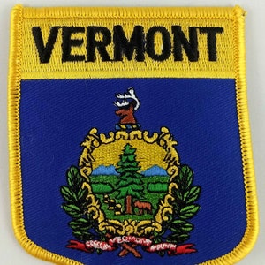May include: Embroidered Vermont state patch with a shield design. The patch features a blue background with the state seal, a yellow border, and the word "VERMONT" in black letters across the top. The seal includes a tree, mountains, and a deer.