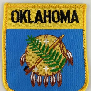 May include: A yellow and blue embroidered patch with the word "OKLAHOMA" in black lettering and the state seal featuring a Native American symbol with a tomahawk and a peace pipe.