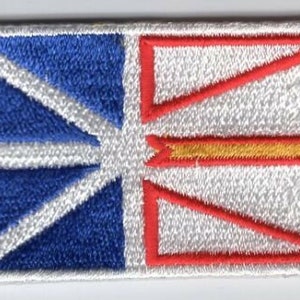 May include: An embroidered patch featuring the flag of Newfoundland and Labrador. The flag is white with a red and yellow cross, and a blue Union Jack in the upper left corner.