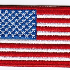 May include: An embroidered American flag patch in red, white and blue. The flag has 13 white stripes and 50 white stars on a blue field.