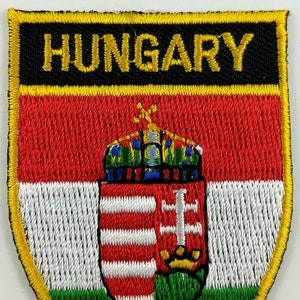 Puede incluir: Parche bordado con el escudo de armas húngaro y la palabra "HUNGRÍA" en letras amarillas sobre fondo negro. El escudo de armas está rodeado por un borde rojo, blanco y verde.