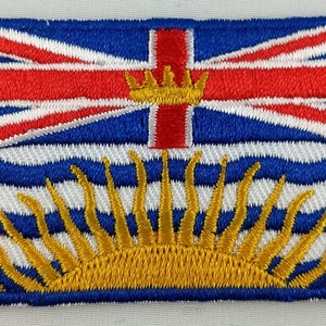 May include: An embroidered patch featuring the flag of British Columbia. The flag is blue with a red cross and a white crown in the center. The bottom half of the flag features a yellow sun with white rays.