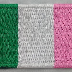 May include: A green, white, and pink embroidered patch. The patch has a white border around the edges.