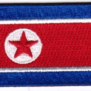 Peut inclure: Un écusson brodé représentant le drapeau de la Corée du Nord. Le drapeau est rouge avec un cercle blanc au centre contenant une étoile rouge à cinq branches.