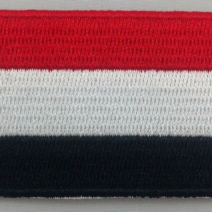 May include: An embroidered patch depicting the flag of Yemen, featuring red, white and black stripes.