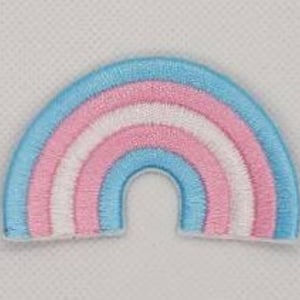 May include: A small embroidered patch in the shape of a rainbow with the colors of the transgender pride flag: light blue, pink, and white.