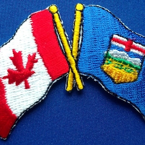 May include: Two embroidered patches, one with the Canadian flag and the other with the flag of Alberta, Canada. The patches are crossed over each other, as if they are on flagpoles.